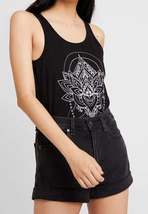 Sort tanktop med hvidt blomstret mandaladesign; båret med sort højtaljede denimshorts. Fokus på enkel, afslappet stil og monokrome farver.