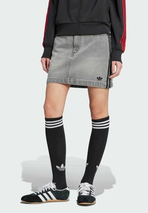 Šedá džínová sukně s bočním rozparkem, s černým logem Adidas. V kombinaci s černými punčochami nad kolena s bílými pruhy a černými sportovními botami.