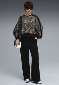 Felpa cropped con stampa leopardata e dettagli neri, abbinata a pantaloni neri a gamba larga e sneakers bianche, completata da una piccola borsa bianca.