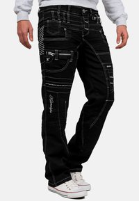 Pantaloni cargo in denim nero con cuciture bianche, molteplici tasche e cerniere. Design affusolato con una leggera texture lavata.