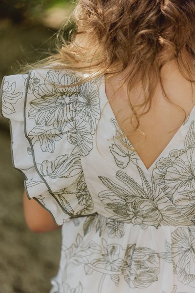 Vit klänning med grön blommönstring, volangärmar och V-formad ryggdesign. Lättviktig tyg med detaljerade blommönster.