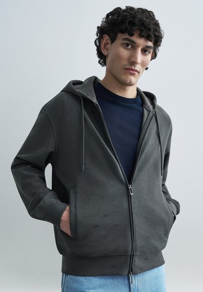 Sweat à capuche gris foncé zippé avec un motif texturé en relief, doté d'une fermeture éclair à l'avant, d'une capuche avec cordon de serrage et de poches kangourou.