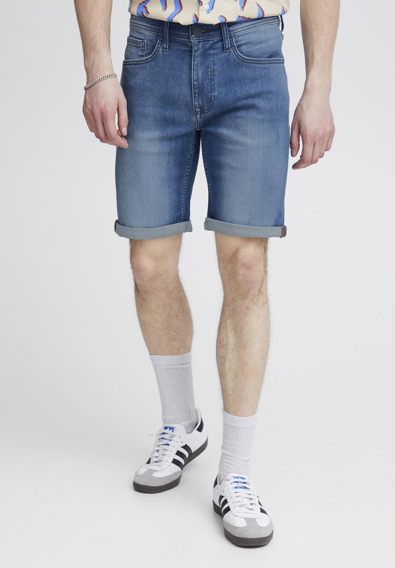 Denims šorti, gaiši zili, ar apgrieztiem malām, piecu kabatu dizains, saskaņoti ar baltām apakšbiksēm un melnbaltām sporta kurpēm.