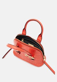 Malá jasně oranžová kabelka s krokodýlí texturou, dvěma ušima, zlatým zipem a otevřeným oddílem, který ukazuje vnitřní kapsu a štítek.