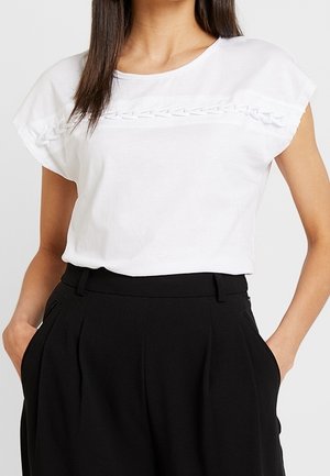 Una camiseta blanca de manga corta con una banda horizontal texturizada en el pecho, combinada con pantalones negros de talle alto.