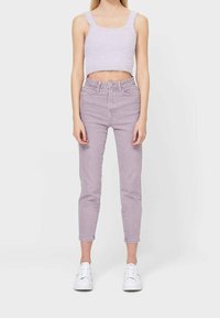 Svetle fialový zkrácený svetr zkombinovaný s vysokými úzkými světle fialovými džíny. Model má na sobě bílé tenisky. Jednoduchý, texturovaný design.