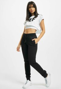 Sorte sweatpants med snøre og sidelommer, parret med en cropped hvid skjorte med et sort grafisk motiv. Hvide sneakers fuldender outfittet.