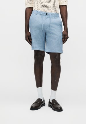 Shorts bleu clair sur mesure en tissu texturé, avec une fermeture éclair et un bouton, des poches latérales et une ceinture ajustable.