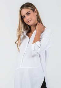 White button-up shirt with long sleeves, side slits, and a relaxed fit, made from a lightweight fabric that drapes smoothly.