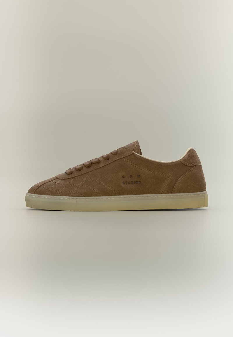 Baskets basses en suède marron avec semelle et lacets beige, estampillées "C.P. Company" sur le côté, présentées sur un fond neutre.