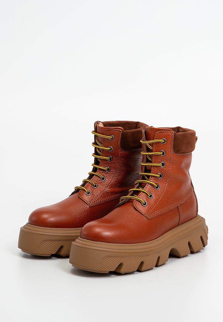 Brown leather ankle boots with a textured finish, yellow laces, and thick, chunky rubber soles featuring a zigzag pattern.