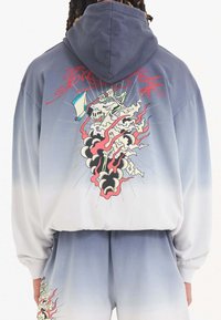 Sudadera con capucha de diseño ombre, que va de gris claro a azul oscuro. Presenta un gráfico de una calavera y llamas en la parte posterior.