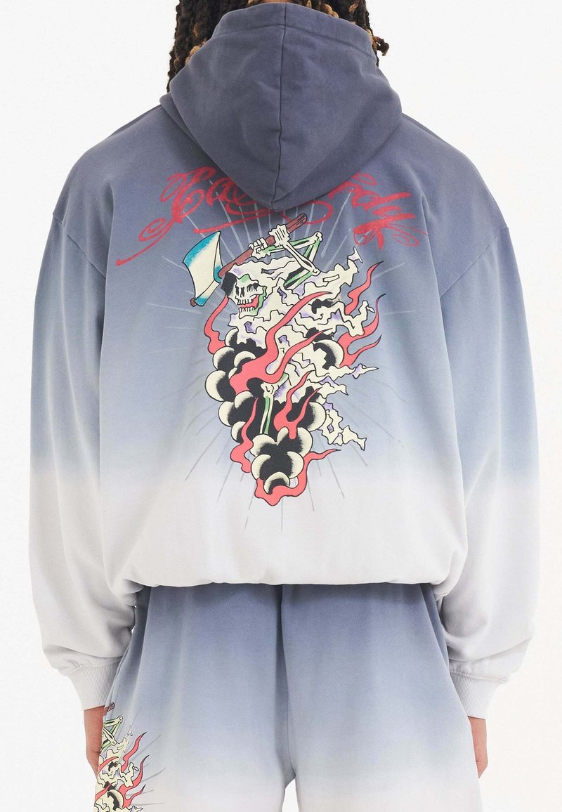 Sudadera con capucha de diseño ombre, que va de gris claro a azul oscuro. Presenta un gráfico de una calavera y llamas en la parte posterior.