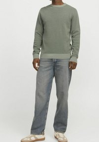 Grön stickad tröja med ett strukturerat mönster, rundad halsringning, ribbade ärmslut, tillsammans med ljusblå denimjeans och beiga sneakers.