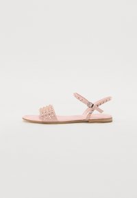 Pink flat sandals with a textured strap featuring decorative studs, adjustable ankle strap, and a flat rubber sole.