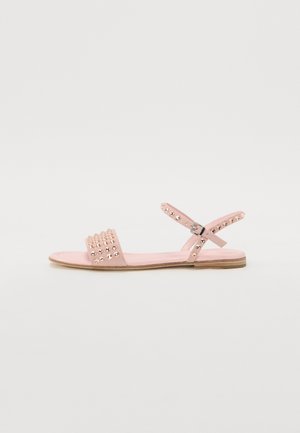 Sandales plates roses avec une sangle texturée ornée de clous décoratifs, une sangle réglable à la cheville et une semelle en caoutchouc plate.