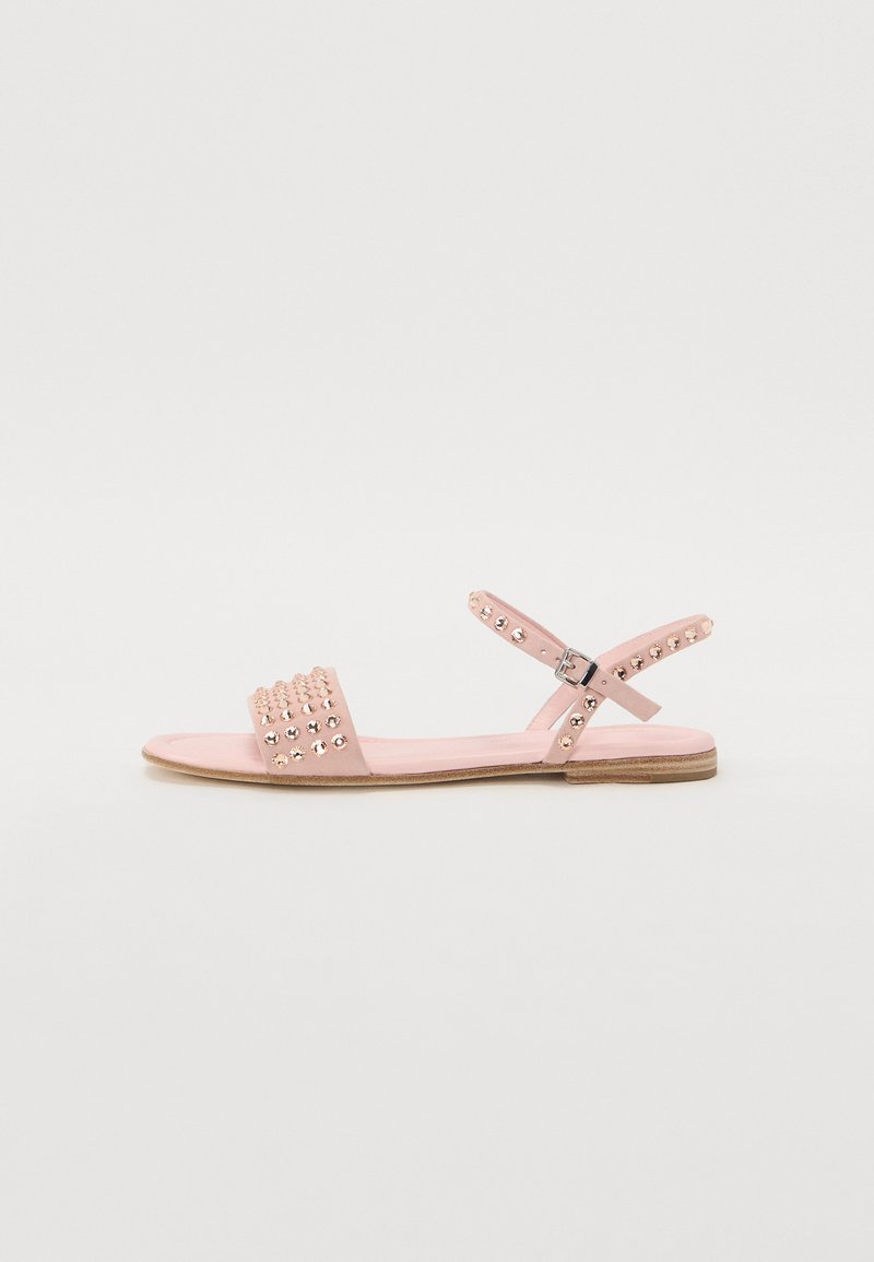 Pink flat sandals with a textured strap featuring decorative studs, adjustable ankle strap, and a flat rubber sole.