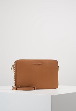 Sac bandoulière rectangulaire en cuir marron avec chaîne dorée et fermeture éclair, posé sur un socle blanc sur fond uni.