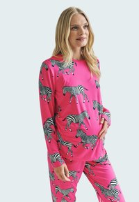 Růžový pyžamový set se zebrovaným vzorem, vyrobený z měkké látky. Dlouhý rukáv a kalhoty až po kotníky, obojí zdobené černobílými zebrami.