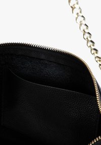 Sort h�åndtaske indvendig med en tekstureret læderfinish. Den har en lynlåslukning og en lomme, foret med blødt materiale. Guld-tonet hardware er synlig.