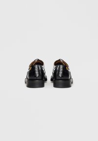 Black leather shoes with a smooth, polished finish, featuring perforated detailing and a round toe. Includes a medium-height heel.
