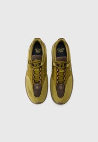 Tênis Nike com uma combinação de cores verde e castanho, materiais em malha e camurça, detalhes perfurados e uma sola de borracha contrastante.
