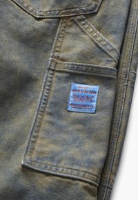 Nogawka spodni dżinsowych z małą boczną kieszenią, na której znajduje się etykieta Levi Strauss & Co. z napisem „kiedy jest dużo do zrobienia”.