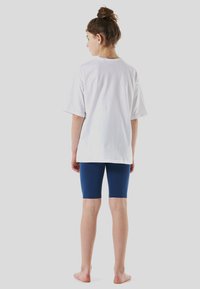 White cotton t-shirt with short sleeves, paired with blue stretchy bike shorts. Simple design, relaxed fit, displayed from the back.