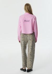 Kort, lichtroze shirt met de tekst "Diamonds" op de achterkant, gecombineerd met beige broek met luipaardprint en zwarte schoenen met metalen accenten.