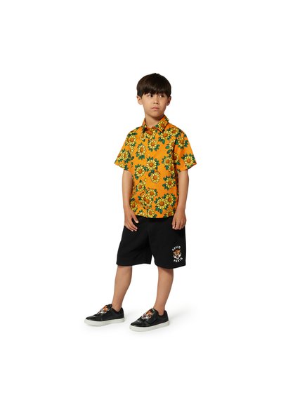 Korte mouwen, feloranje overhemd met zonnebloemprint; gecombineerd met zwarte short met een tijgerontwerp en zwarte sneakers.