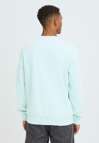 Světle modrá mikina s kulatým výstřihem, vyrobená z měkké látky, s dlouhými rukávy a volným střihem. Minimální značení na lemu.