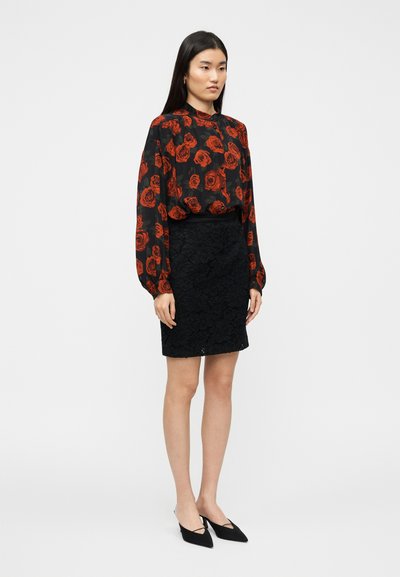 Blouse noire imprimée de roses rouges, associée à une jupe en dentelle noire. Comprend des manches longues, une devanture boutonnée et des escarpins noirs à bouts pointus.