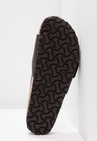 Černá gumová podrážka obuvi s texturovaným vzorem propojených kruhů, odhalující horní okraj připomínající korek.