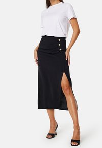 Mustan keskipitkän hameen, jossa on sivuaukko, rypytetty yksityiskohta ja kolme kultasävyistä nappia. Yhdistetty valkoiseen t-paitaan ja korkokenkiin.