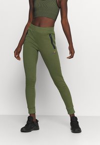 Grønne sweatpants med sidelommer med lynlås, tæt pasform, ribbet talje og afsluttede ankler. Kombineret med en matchende cropped top og sorte sneakers.