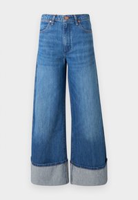 Jeans de mezclilla de pierna ancha en azul medio. Presentan una cintura alta, dobladillos acampanados en mezclilla más clara y un diseño clásico de cinco bolsillos con acentos metálicos.