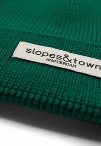 Zielona czapka dzianinowa z teksturowanym wzorem. Metka z napisem "slopes&town AMSTERDAM" na kremowej etykietce przyszytej do materiału.
