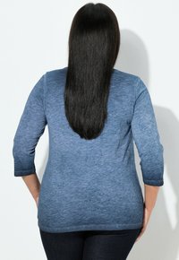 Niebieska koszula z długim rękawem o długości 3/4, z teksturowanej tkaniny, gładkim wykończeniem i zaokrąglonym dołem, w połączeniu z ciemnymi jeansami.