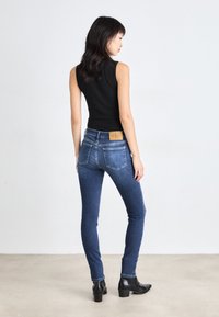 Μπλε τζιν skinny παντελόνι με ελαφριά φθορά, τονισμένες πίσω τσέπες και δερμάτινη ετικέτα. Μαύρη εφαρμοστή αμάνικη μπλούζα και μποτάκια μέχρι τον αστράγαλο.