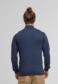 Mörkblå stickad tröja med hög krage, långa ärmar och ribbade muddar. Slät textur, åtsittande design och minimal detaljer.