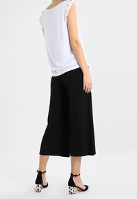 Top bianco a maniche corte con orli arricciati, abbinato a culotte nere. Le calzature presentano una base nera con tacchi a pois.