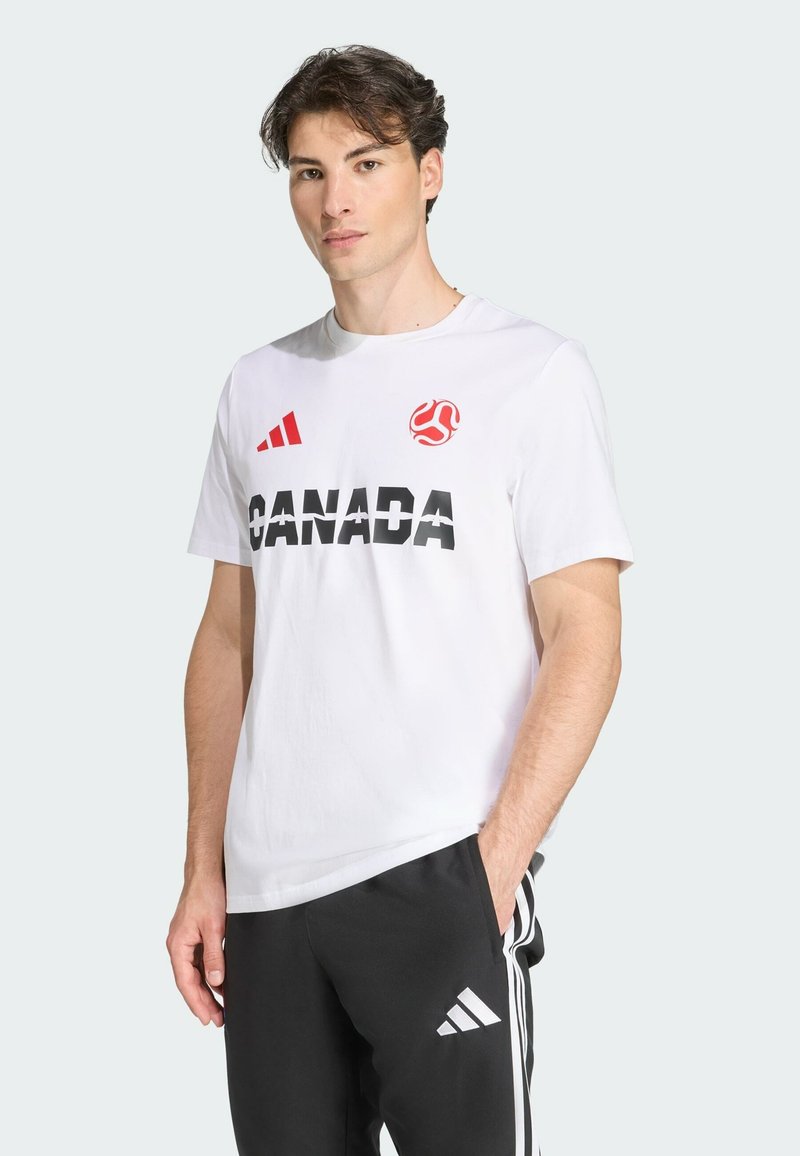 Camiseta blanca de algodón con el destacado texto negro "CANADÁ", acentos rojos y un logo. Combinada con pantalones negros que presentan rayas blancas.
