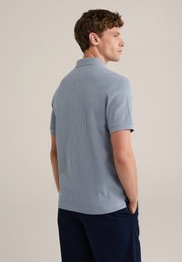 Polo din bumbac de culoare bleu deschis, cu un croi slim, mâneci scurte și guler clasic. Textura materialului pare moale și respirabil.