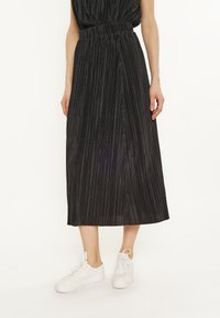 Gonna midi plissettata nera con vita elastica, indossata con sneakers bianche. Il tessuto ha una superficie liscia e righe verticali.