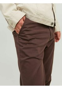 Brown cotton trousers with a smooth texture and tailored fit, paired with a light beige shirt featuring button details and cuff.