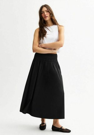Zwarte maxi rok van lichtgewicht stof, met een smocked tailleband voor comfort. Gepaard met een eenvoudige witte mouwloze top en platte schoenen.