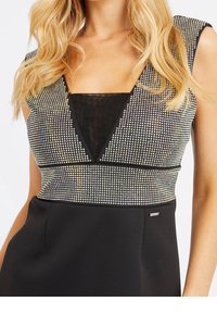 Robe noire avec un décolleté en V profond, ornée de strass argentés sur le buste. Tissu lisse avec une coupe ajustée.