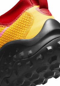 Scarpa sportiva con tomaia in mesh rosso e giallo, dotata di suola in gomma nera texturizzata e di impronte sagomate distintive per la trazione.
