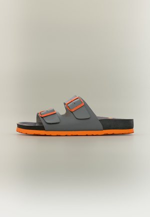 Grå sandal med to spænderemme og en orange sål, vist i profil på en ensfarvet baggrund. Ingen personer til stede.