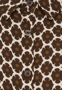 Brun blomsterprintet stof med store mørkebrune blomster med sennepsfarvede midter, fem knapper og et klassisk kravesnit.